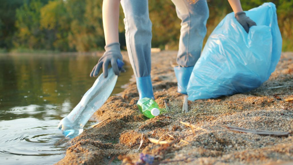 A gloved hand picking a plastic bottle out of shallow water
