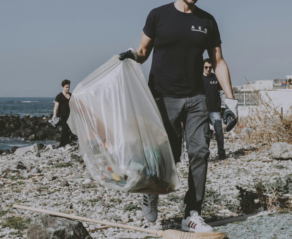 A volunteer carrying a full bag of collected litter across a rocky shore