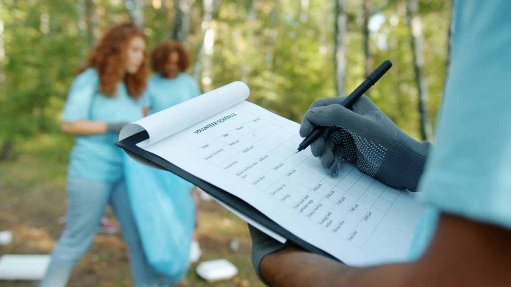 A gloved hand ticking off a checklist on a clipboard during an outdoor cleanup