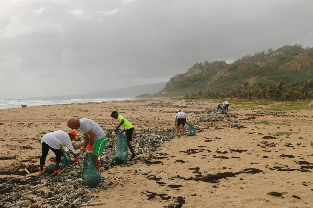 People picking up litter along a wide sandy beach under an overcast sky