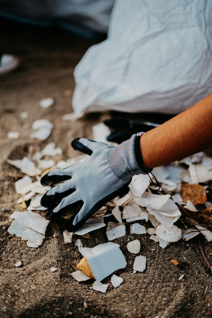 Close-up of a gloved hand and a litter picker lifting shards of broken glass from the ground