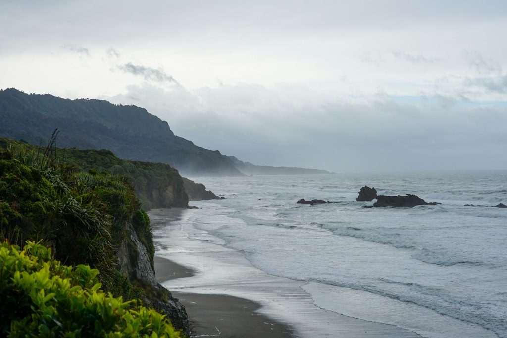 Waves rolling onto a long beach beneath dark cliffs and a cloudy sky