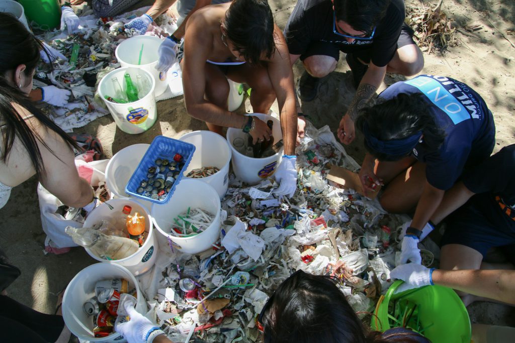 Volunteers kneeling around buckets, sorting plastic and debris collected from a beach